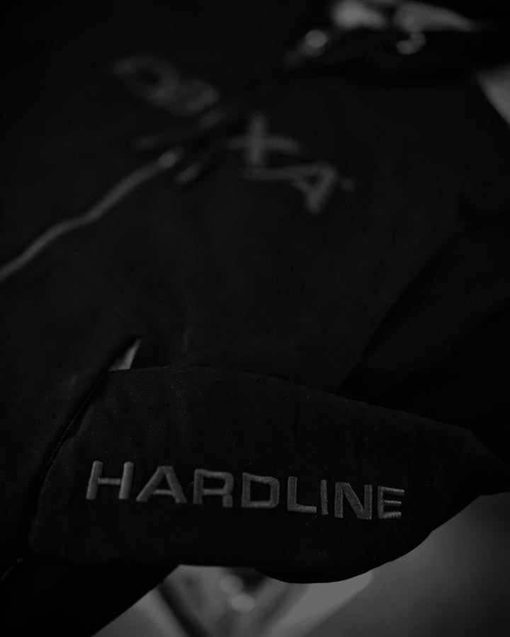 Close-up of HARDLINE sleeve embroidery on the black DBXA Ironveil hoodie.