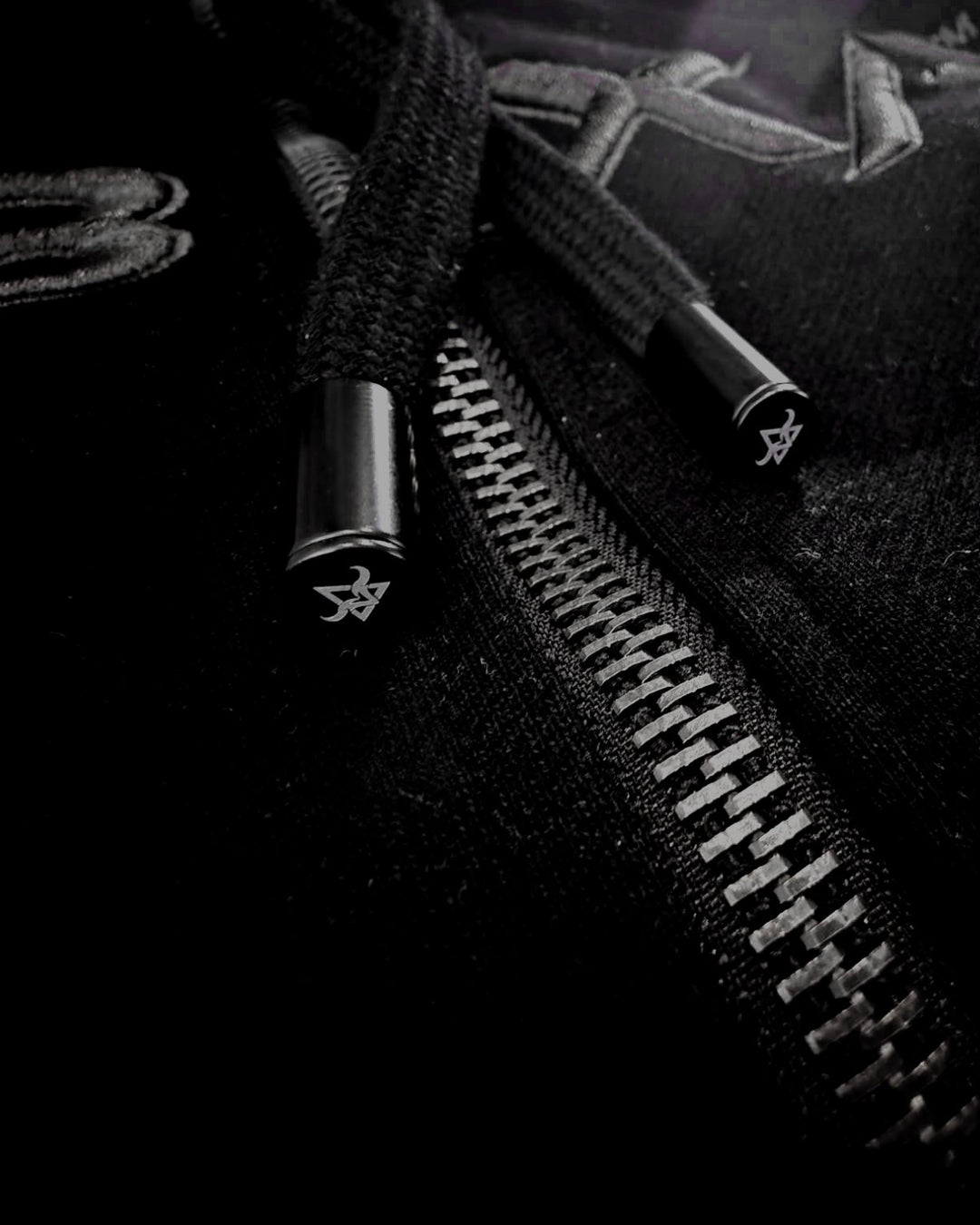 Close-up of black drawcords and silver zip hardware on the DBXA Ironveil hoodie.