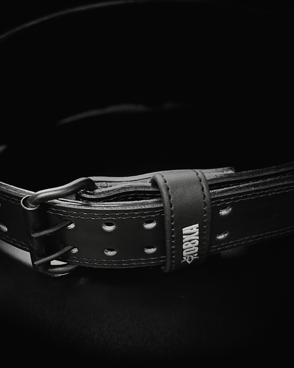 Black leather belt with visible branding on a dark background