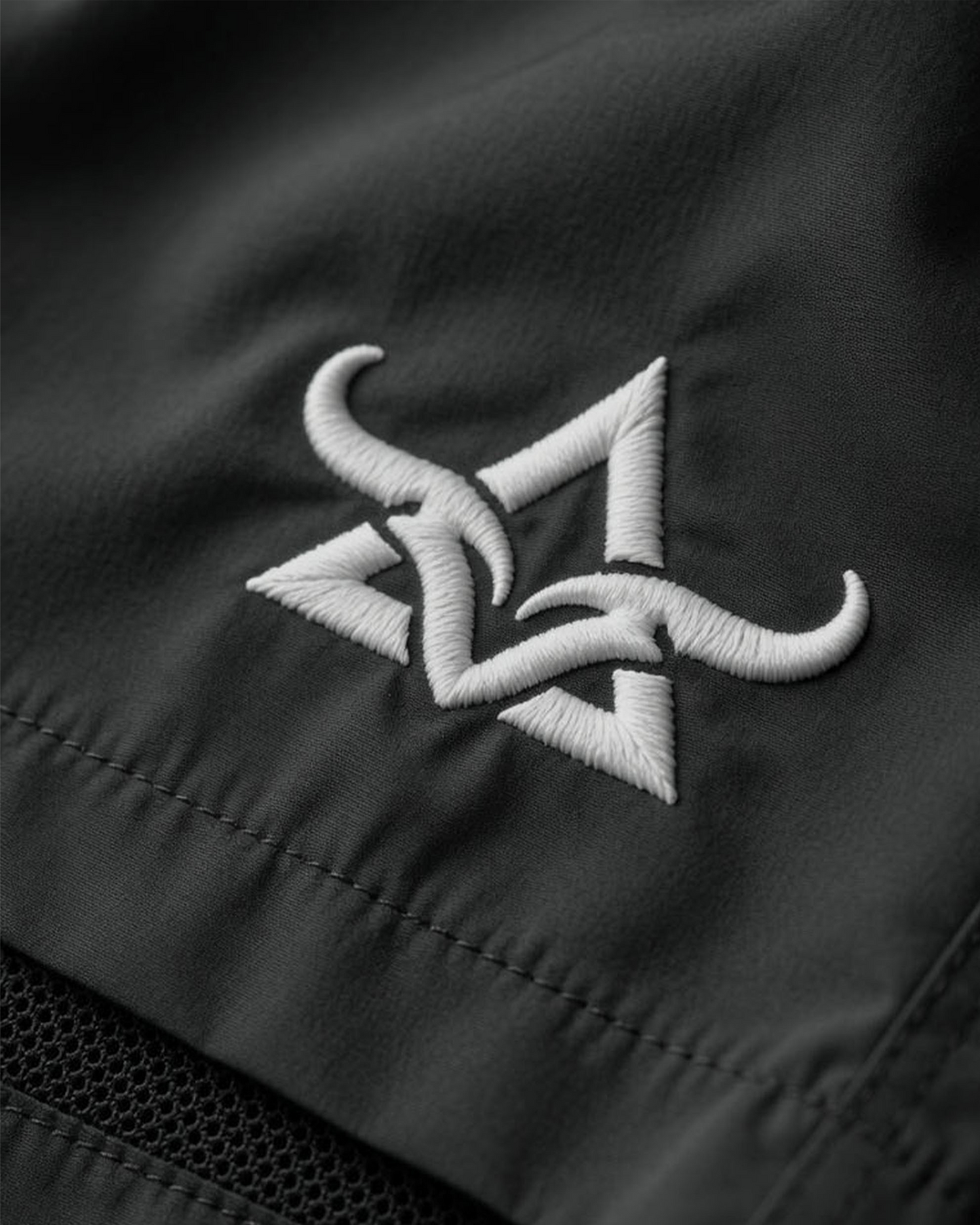 Close-up of a black shorts with a white embroidered logo on a dark background