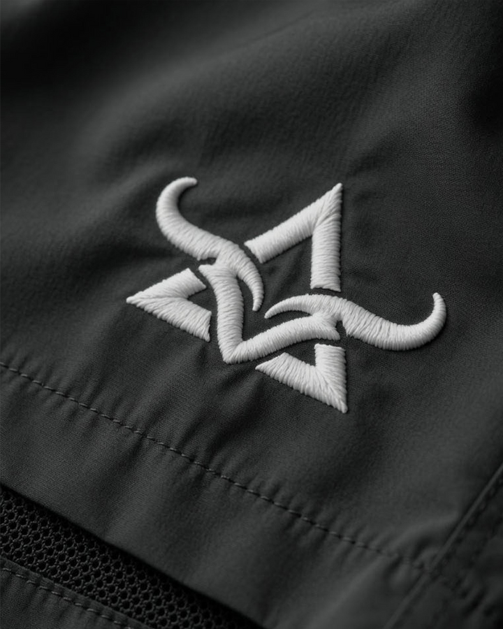 Close-up of a black shorts with a white embroidered logo on a dark background