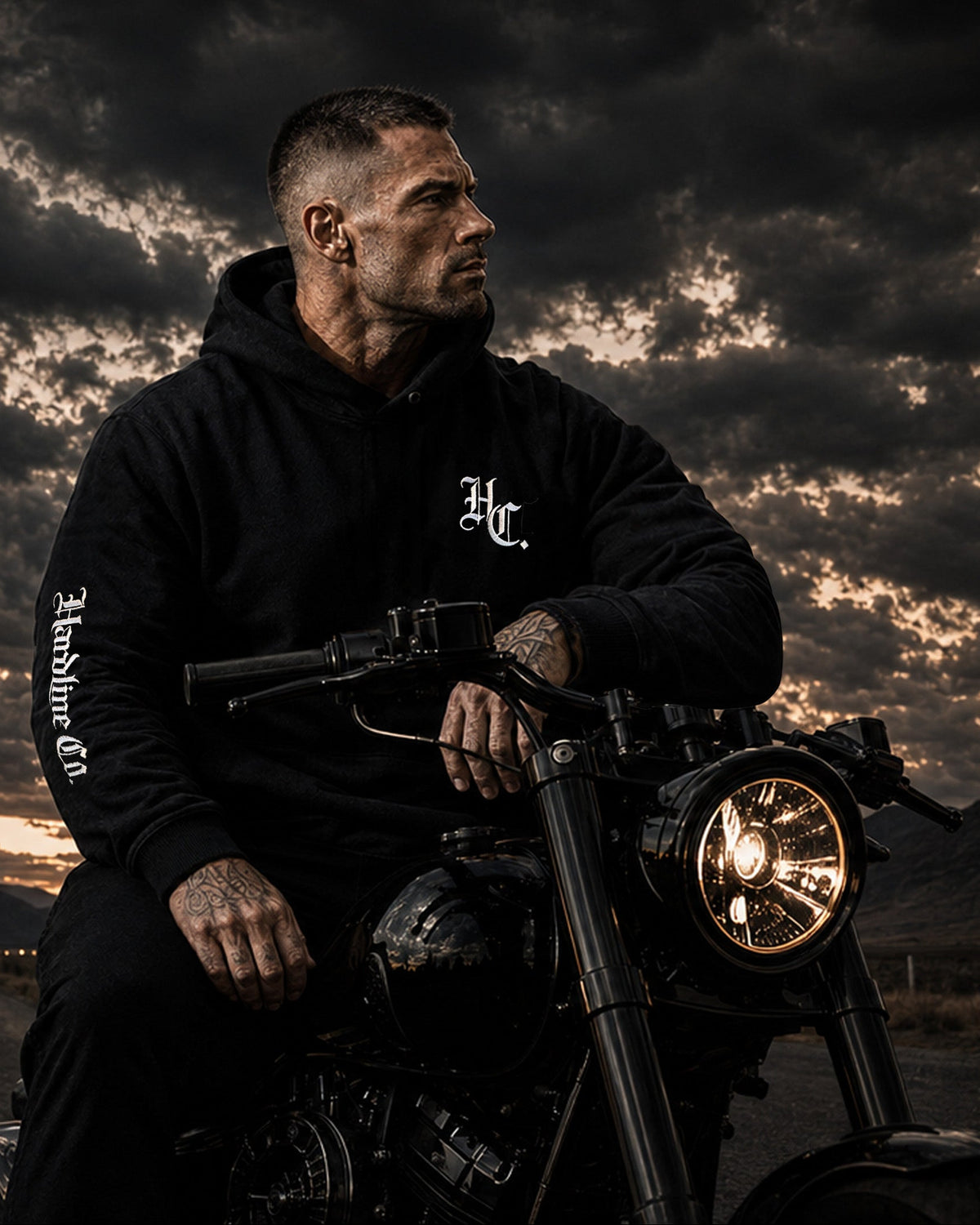 A man wearing a black hoodie with a white 'Hardline Co' logo sits on a cruiser motorcycle on a dark road under a dramatic cloudy sky. Large 'Hardline Co' branding and tagline text are overlaid on the left side of the image.