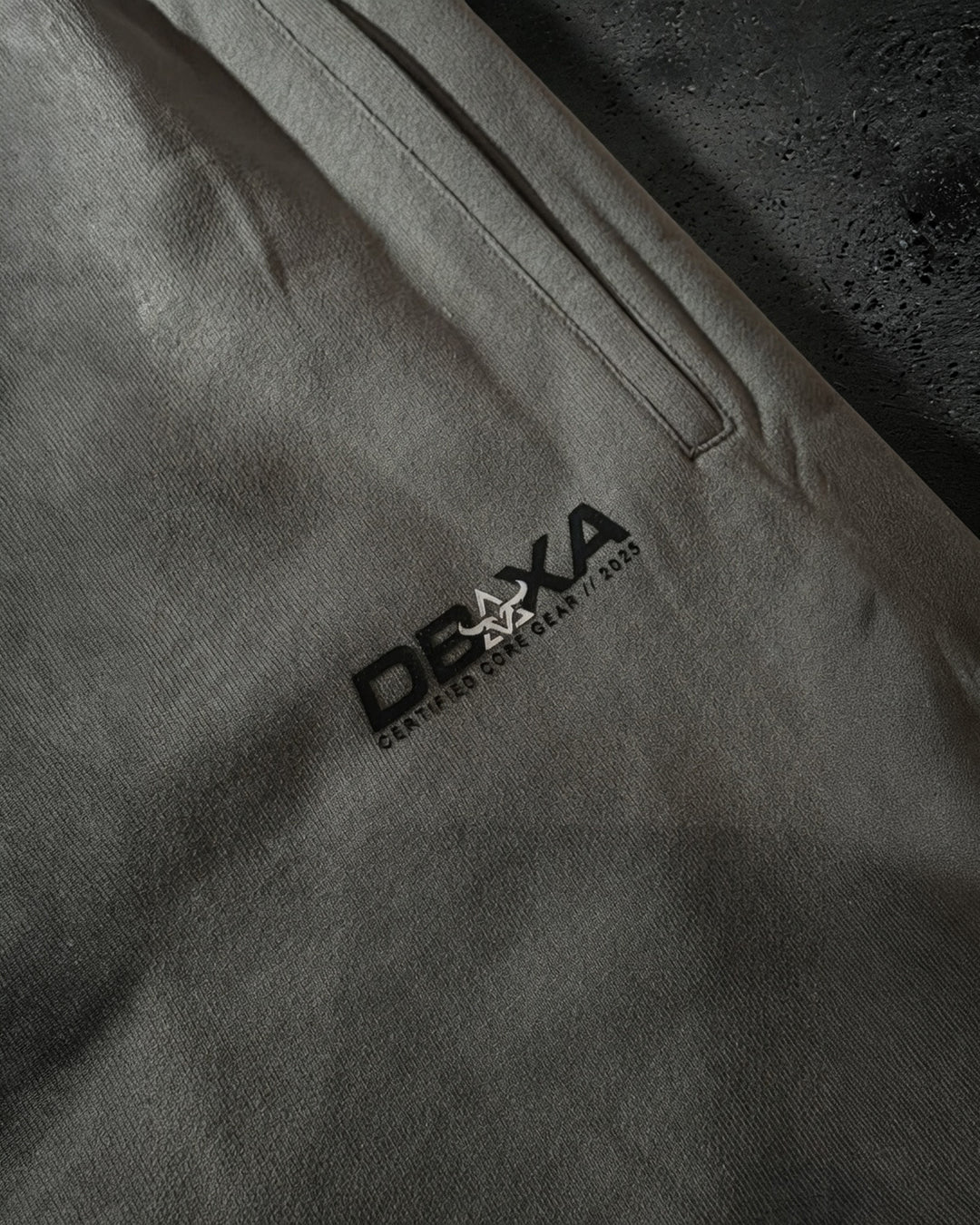 Close-up of a gray pants pocket area with a brand logo on a tdark gray pair of pants