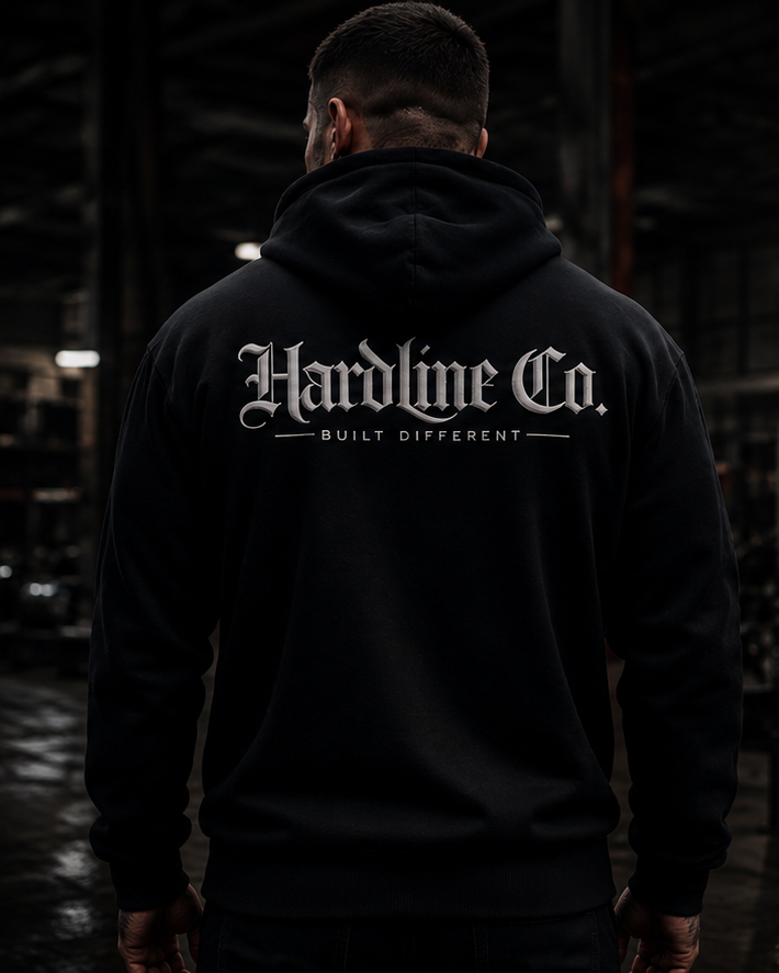 Two men wearing black pullover hoodies in a dark gym interior. One man faces forward showing a white 'HC' logo on the left chest and 'Hardline Co.