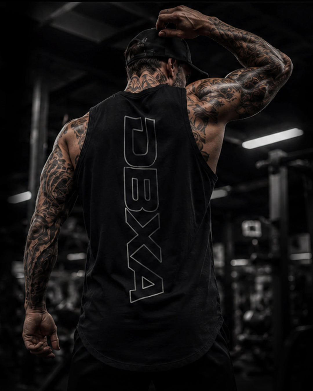 Person wearing a black sleeveless shirt with 'DBXA' logo in a gym setting