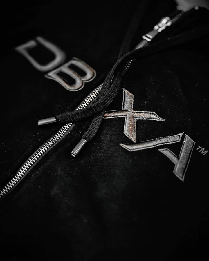 Close-up of metallic DBXA embroidery and silver zip hardware on the black Ironveil hoodie.