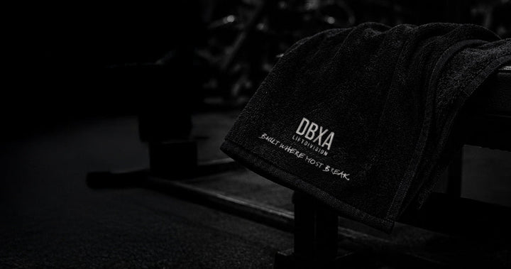 Wide product view of the black DBXA Lift Division gym towel on a bench