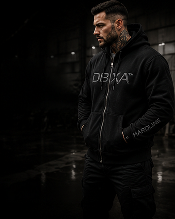 Male model wearing the black DBXA Ironveil zip hoodie in a dark industrial setting.