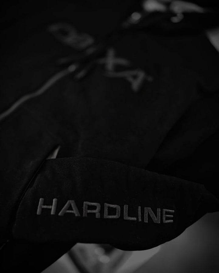 Close-up of HARDLINE sleeve embroidery on the black DBXA Ironveil hoodie.