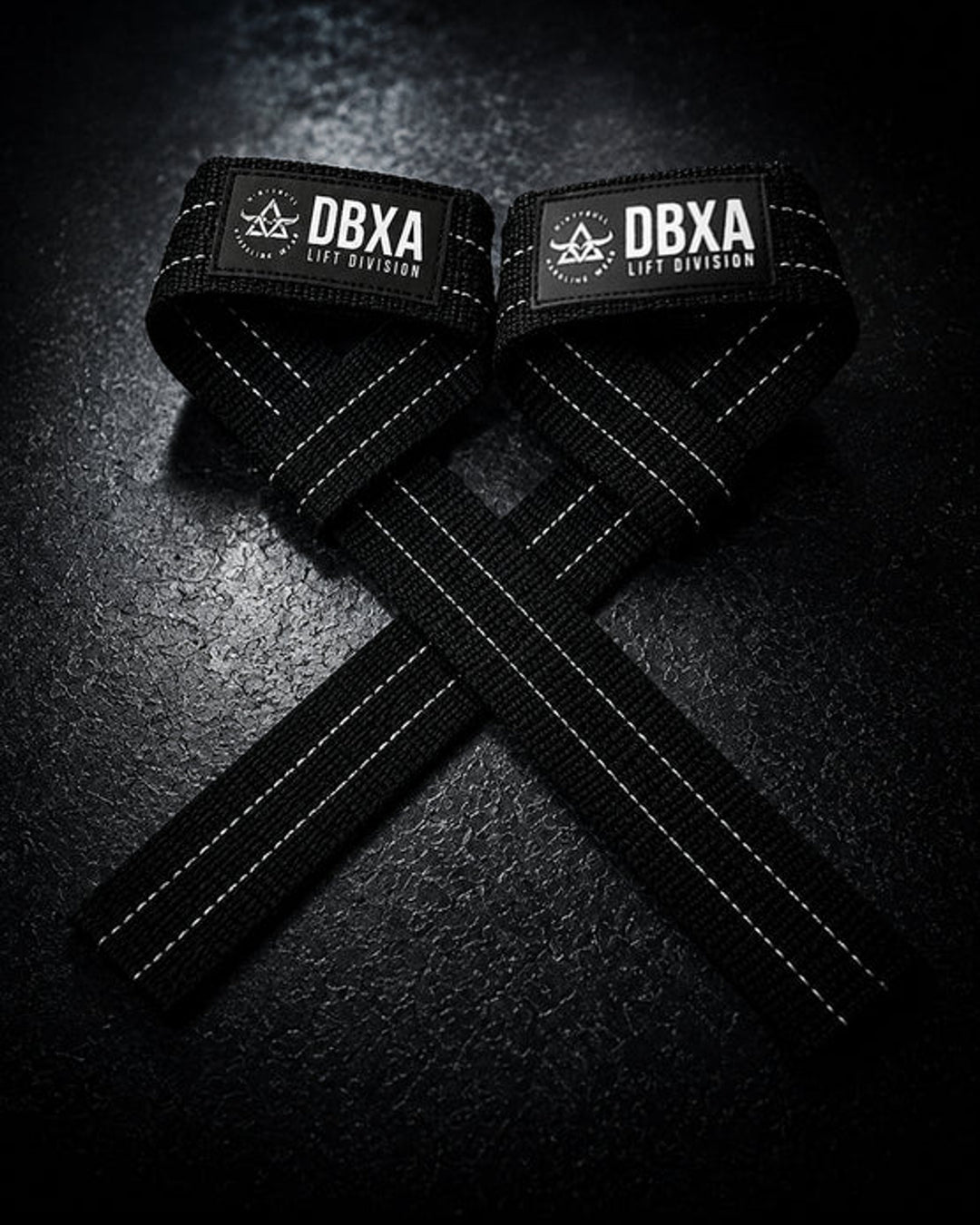 Black DBXA lifting straps crossed on a dark surface