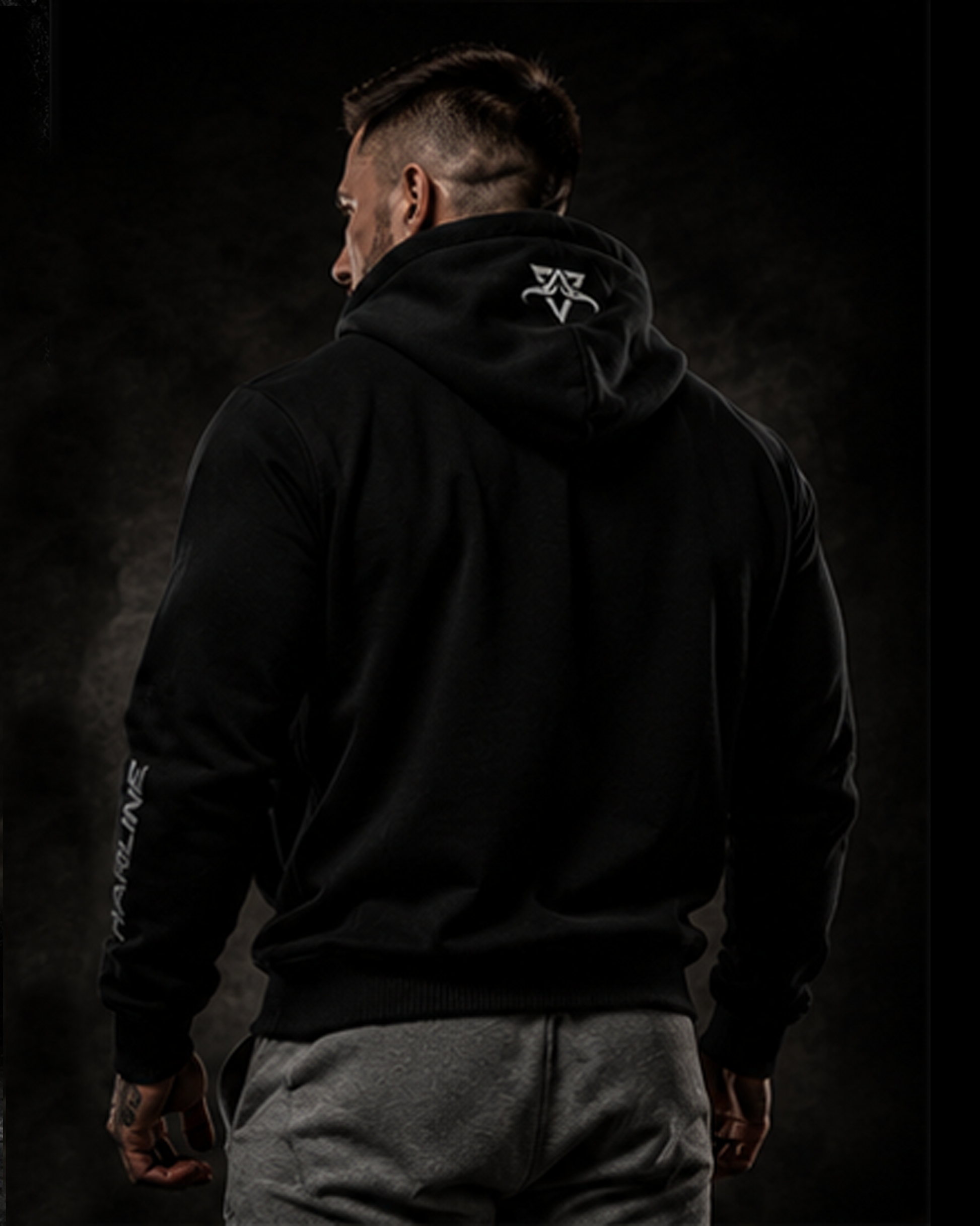 Person wearing a black hoodie with a logo on the back against a dark background