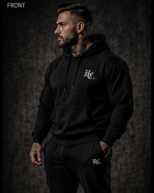 Man wearing a black hoodie and pants with a logo, standing against a dark background