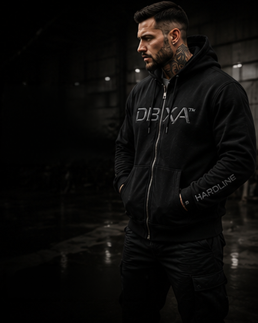 Male model wearing the black DBXA Ironveil zip hoodie in a dark industrial setting.